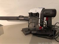Side view of Dyson cordless vacuum connected to charger cable, showing dustbin and handle.