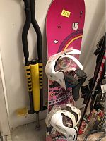 Burton snowboard with white bindings standing upright against wall next to yellow and black pogo stick.
