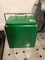 Front view of green metal ice chest with silver corner reinforcements and handle on top.