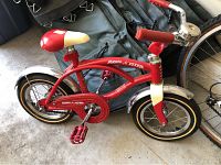 Side view of red Radio Flyer child's bicycle showing frame, seat, pedals, and wheels.