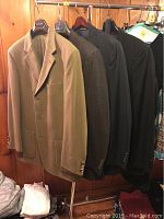 Five men's suit jackets and blazers hanging on rack including beige, charcoal, check, pinstripe and black