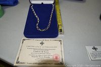 Necklace laid inside open blue velvet box with certificate of authenticity and measuring tape alongside showing length