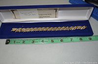 Gold and silver tone bracelet inside blue velvet-lined box with a measuring tape showing about 8.5 inches length.