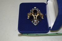 Gold-tone brooch with black and clear rhinestones in blue velvet jewelry box with measuring tape for scale.