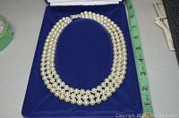 Triple strand faux pearl necklace inside blue fabric-lined box, showing approximate 17 inch length.