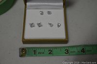 Set of three pairs of clear stone stud earrings displayed in white velvet jewelry box, includes varying shapes and sizes, placed with a measuring tape for scale