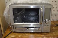 Front view of stainless steel Wolfgang Puck digital convection oven with glass door and handles, taped for shipping.