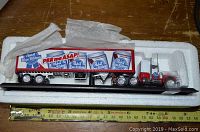 Side view of die-cast Peterbilt truck and trailer featuring Pabst Blue Ribbon design, displayed in white foam packaging on wooden surface next to measuring tape for scale.