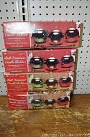 Four unopened red boxes labeled 'Ball Ornament Candle Holders' stacked on shelf, each with image of three ceramic ball holders with votive candles on top.