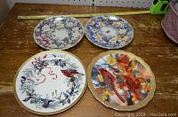 Photo showing four collector plates with floral and bird themes, two with cardinals, others with floral wreaths and bird designs.