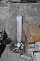 Bissell SpotBot carpet cleaner alongside Honeywell vertical fan against a concrete wall with some boxes.