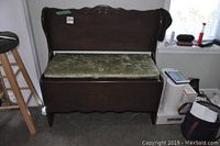 Full front view of dark wooden bench with carved backrest and green padded seat showing storage feature.
