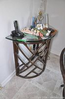 Side view of half circle glass topped side table showing items on top including a cordless phone, decorative figurines, and an oil lamp. Wooden lattice base visible.