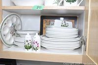 Wood cabinet shelf with stacked white porcelain plates, bowls, covered butter dish, salt and pepper shakers