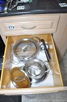 Three pots with matching lids and potato ricer arranged in a wooden drawer