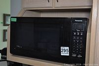 Front view of Panasonic black microwave oven with closed door and visible MaxSold lot sticker