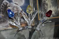 Front view of three Swarovski crystal tulips mounted on a curved silver-colored band: blue, yellow, and red crystal flowers with clear crystal leaves.