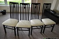 Front view showing four black chairs with white upholstered seats aligned in a row.