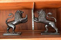 Pair of dark brown carved stone lion book ends facing each other on a wooden shelf, showing front and side profile.