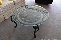 Full view of the round glass coffee table showing the metal frame with a flower petal design in the center and curved legs.