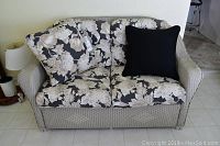 Full view of love seat wicker couch with floral cushions and one solid black cushion