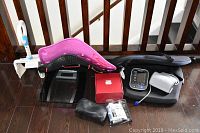 Lot contents showing two Dr. Ho's chair back supports (black and pink), Weight Watchers glass scale, Omron blood pressure monitor with cuff, Silk'n box, and foot/personal care wands.