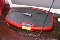 Red Vibra Fit vibrating fitness platform with cords and handheld remote on platform.