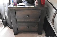 Front view of a dark wood night table showing two drawers with round knobs and weathered finish.