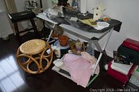 Collapsible metal desk and wicker stool with various household items around and on the desk.