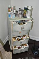 Cabinet with drawers open showing multiple paint bottles inside and two bunny sculptures on top