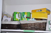 Shelf with wicker baskets containing cleaning supplies, Swiffer replacement pads, Philips light bulb box, and assorted household items.