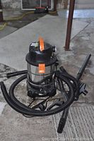 Rigid shop vac with attached coiled hose and multiple cleaning attachments on concrete floor.