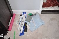 Top down view of Verilux UV wand, collapsible blue hair dryer, white handheld massager, heating pad with wired controller, pink foam roller, and small fabric pouch arranged on carpet