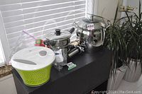 Large Lagostina pots and a salad spinner on black table by window