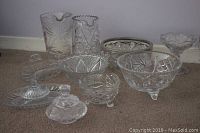 Wide view of the 10-piece glass and crystal set laid on carpet showing variety of pitchers, bowls, and serving dishes with distinct cut crystal patterns.