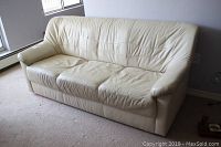 Ivory leather 3-seater sofa seen from an angle showing wear, creasing on cushions and arms.
