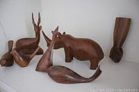Group of 7 carved wooden animal figures and a fist sculpture shown on a white surface. Items include whale, rhinoceros, antelope, birds, and a wooden fist detail.