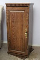 Front view of wood grained solid door side of the revolving cabinet showing decorative molding and brass-tone handle