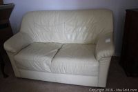 Front view of ivory leather love seat, showing two seat cushions and upright back with wear visible on cushions.
