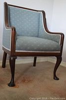 Front and side view photo showing curved wood frame and upholstered seat and back of occasional chair with cabriole Queen Anne legs and puddle feet.