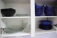 Shelf with black square bowls, clear glass plates, clear glass cups.