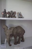 Four elephant figurines displayed on shelving, one large and three smaller.