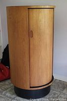 Front view of closed cabinet showing teak veneer tambour door, recessed handle, round top and black base