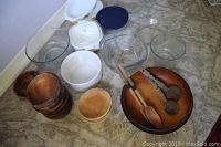 Multiple glass bowls, white covered CorningWare casserole, blue lid, amber Pyrex bowl, wooden salad bowls, and wooden serving utensils grouped on floor.