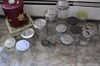 View of all four graduated glass canisters with metal lids alongside multiple smaller canning jars and two vintage floral tins on a tiled surface.