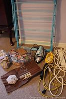 Photo showing the metal folding drying rack, steam iron, sewing threads, extension cords, and sewing notions assembled on the floor.