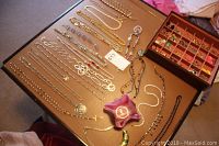 Wide view of the table surface showing an assortment of gold-tone and silver-tone necklaces and pendants laid out flat.