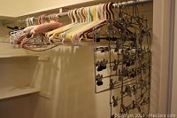 Wide shot of closet rod densely packed with a mix of pastel plastic hangers, pink padded hangers, and multiple metal clip hangers with several clips each.