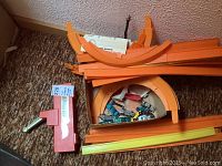 Overview photo of box with orange Rod Runner track pieces, red blaster launcher, instructions, and assortment of Hot Wheels cars.