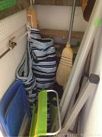 Photo showing folded lawn chairs, brooms, and striped leather wood carrier in a bag near a wall with a water faucet.